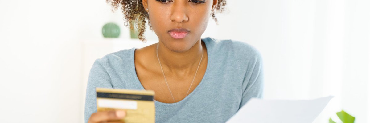 A young woman with a serious look on her face stares at her credit card.