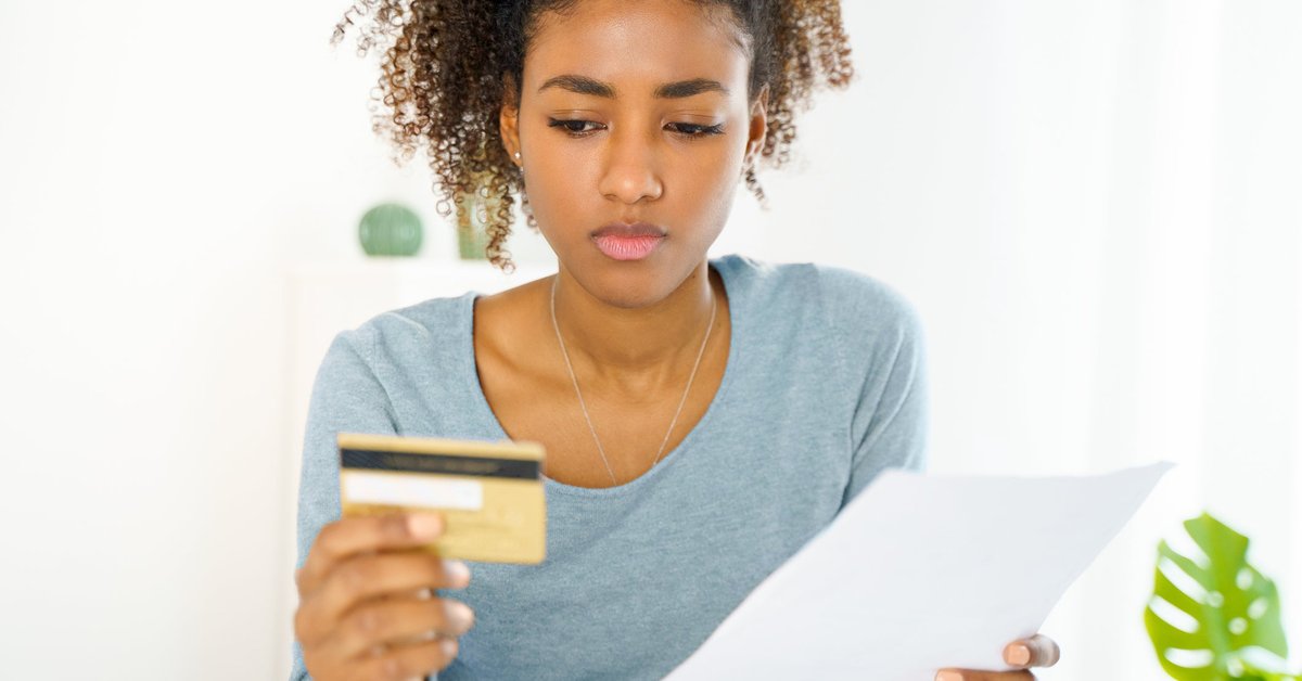 A young woman with a serious look on her face stares at her credit card.