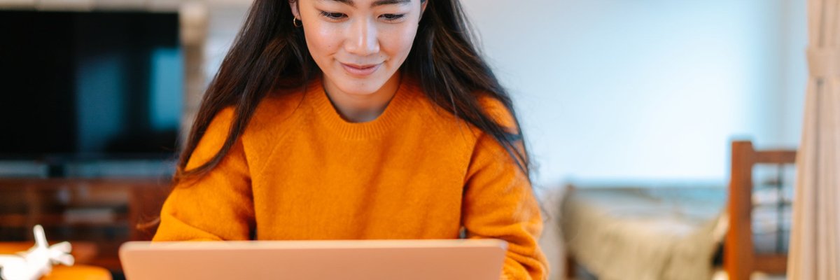 A young woman sits at home, looking at her laptop.