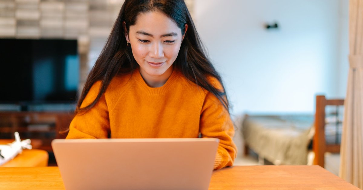 A young woman sits at home, looking at her laptop.