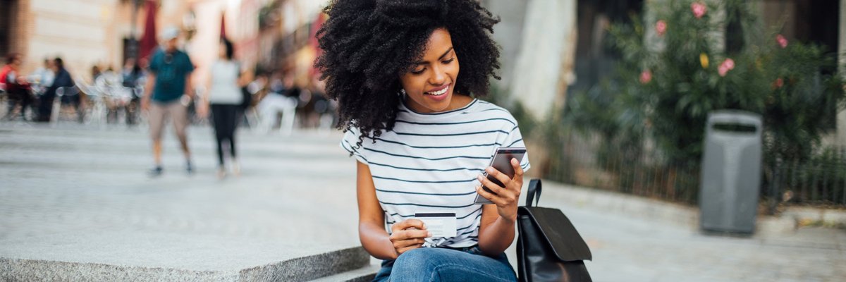 A young woman makes an online purchase while sitting outside.
