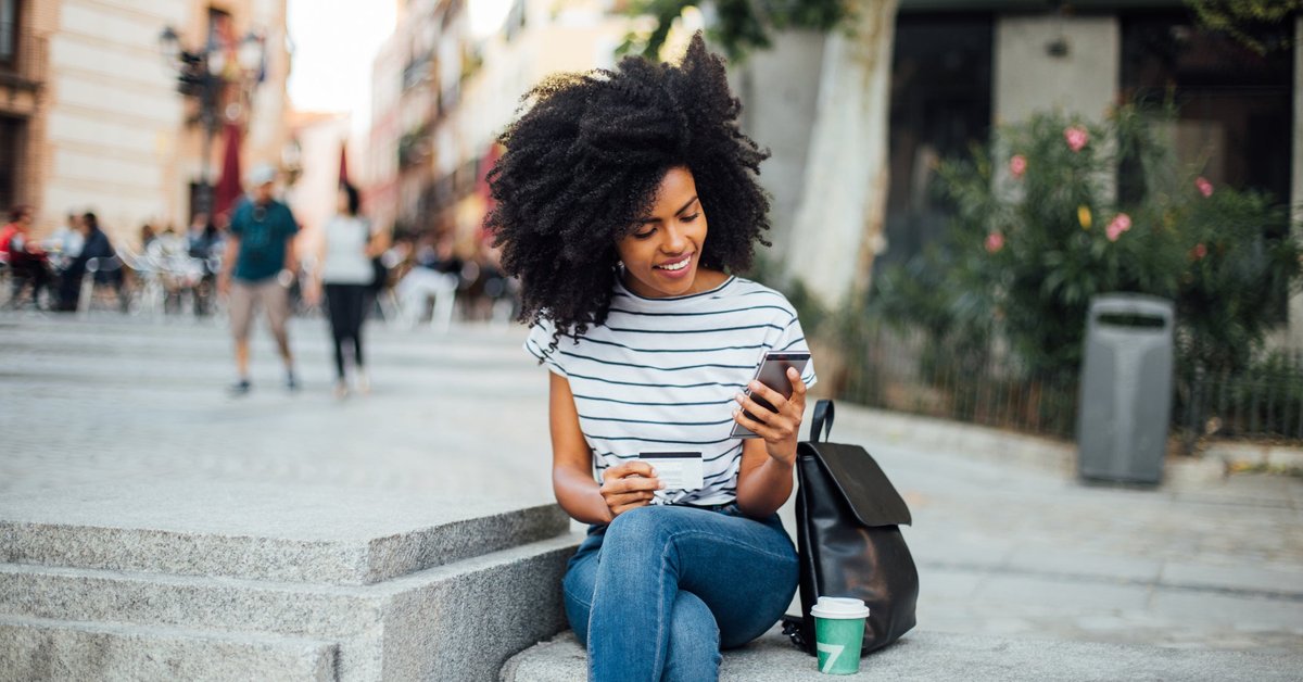 A young woman makes an online purchase while sitting outside.