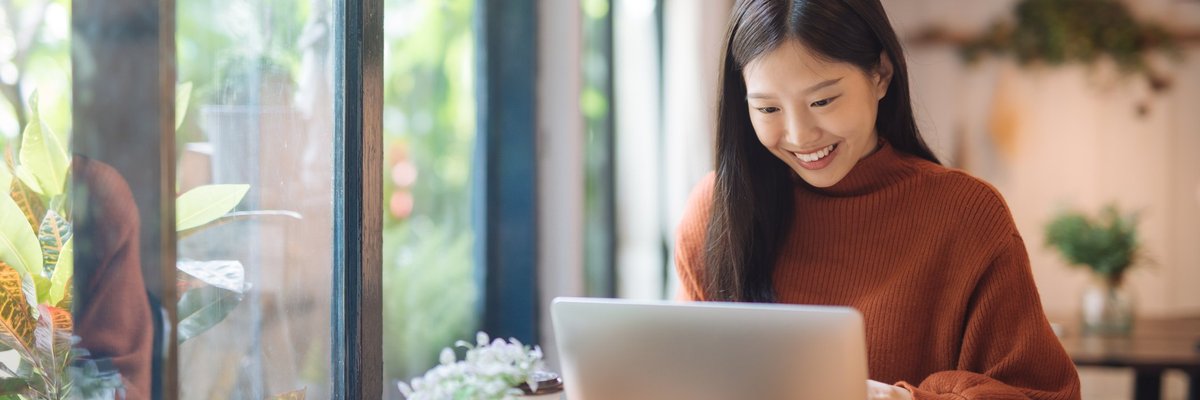 A young woman working on a laptop in a sunny cafe.