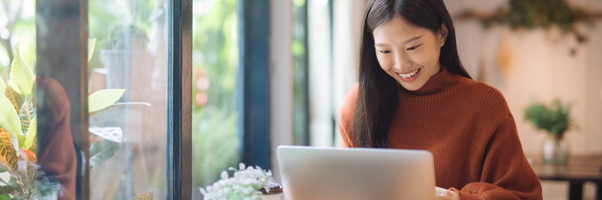 A young woman working on a laptop in a sunny cafe.