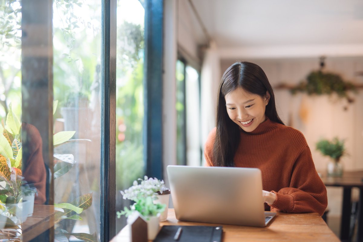 A young woman working on a laptop in a sunny cafe.