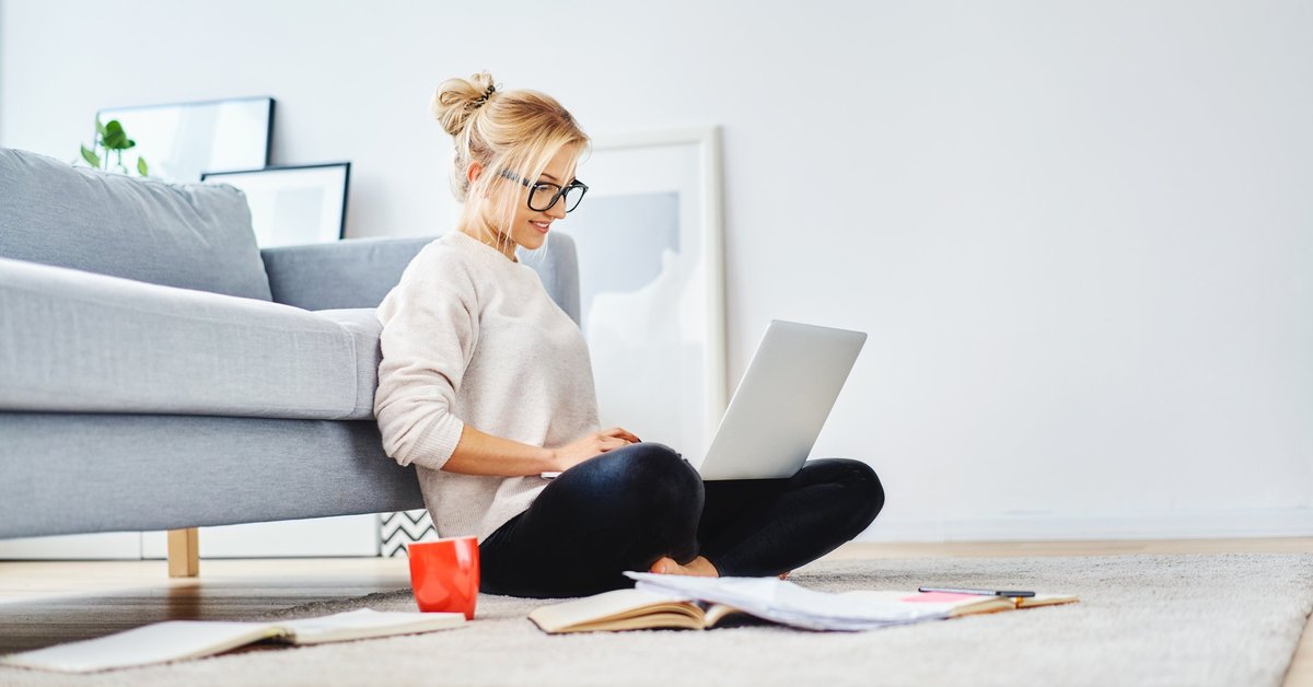 A young woman sitting on the floor working on her laptop.