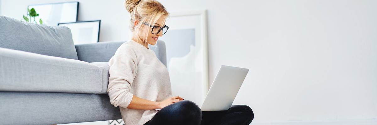 A young woman sitting on the floor working on her laptop.