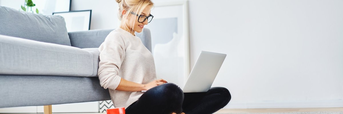 A young woman sitting on the floor working on her laptop.