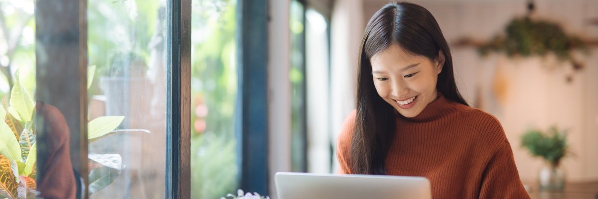 A young woman working on a laptop in a sunny cafe.