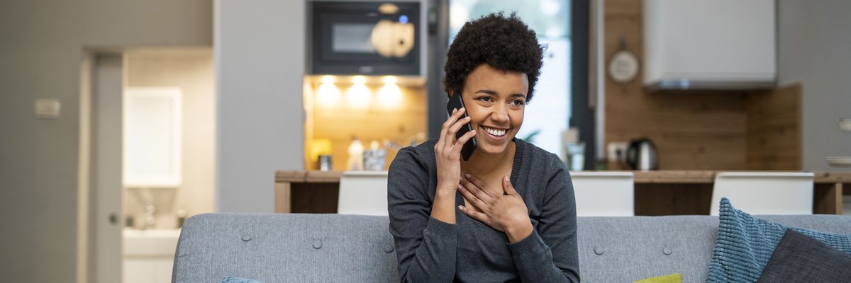 Young woman sitting on couch talking on phone with look of relief.
