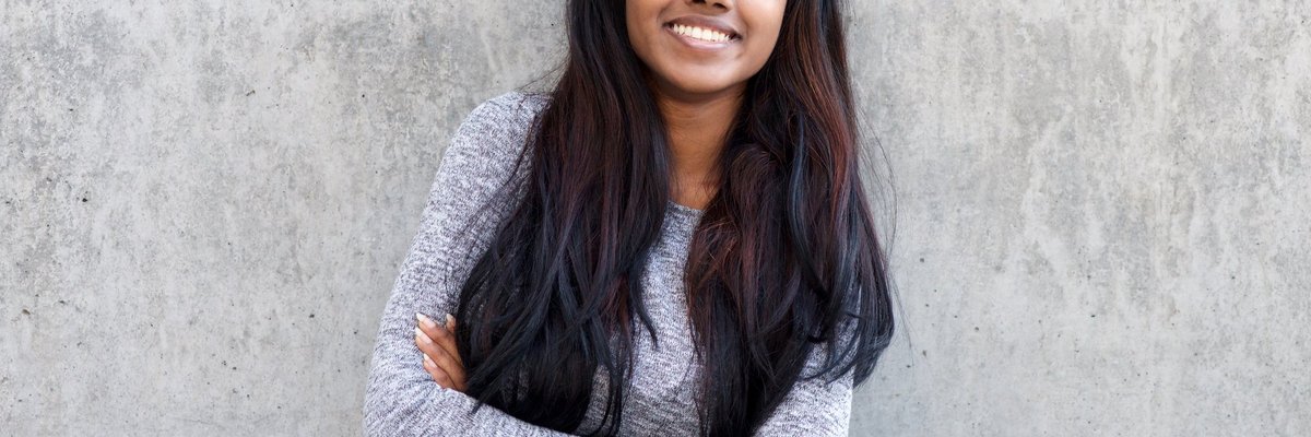 A smiling young woman leaning against a wall.