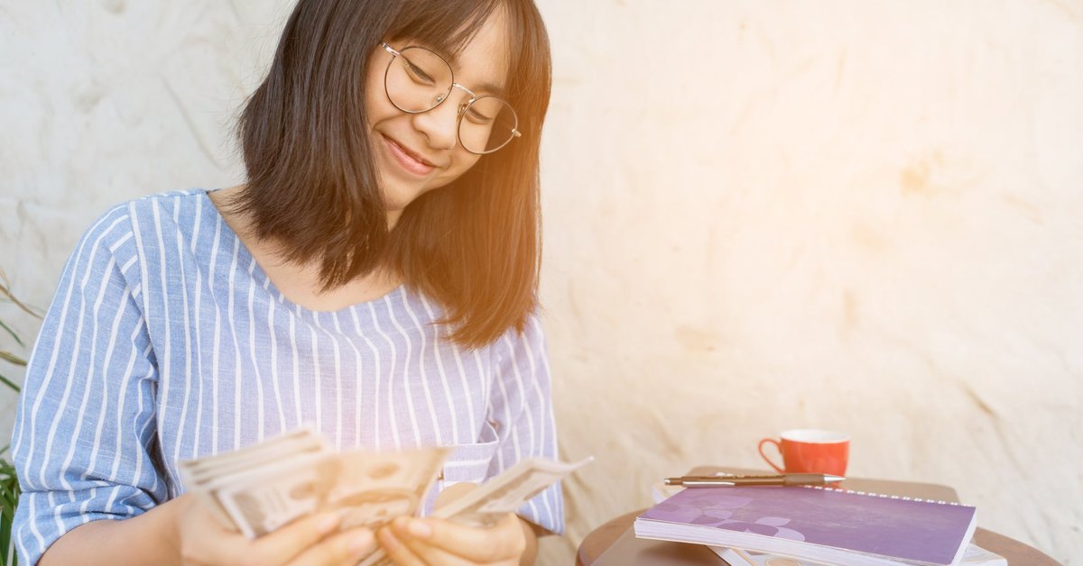 Young woman smiling as she counts cash in her hands.
