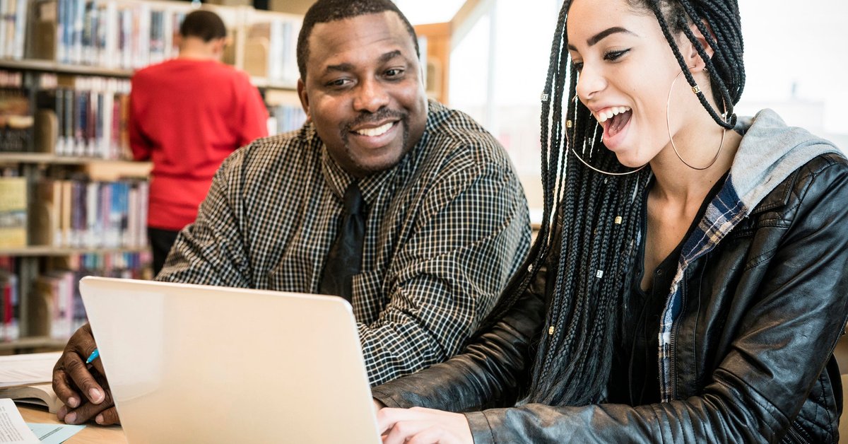 Young woman smiling using laptop next to adult male in a library.