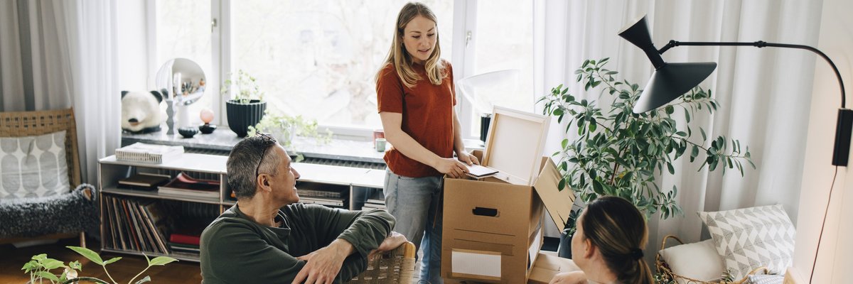 Young woman talking with parents while unpacking box in living room at home.