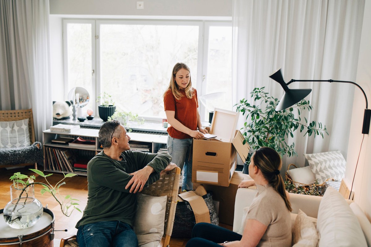 Young woman talking with parents while unpacking box in living room at home.