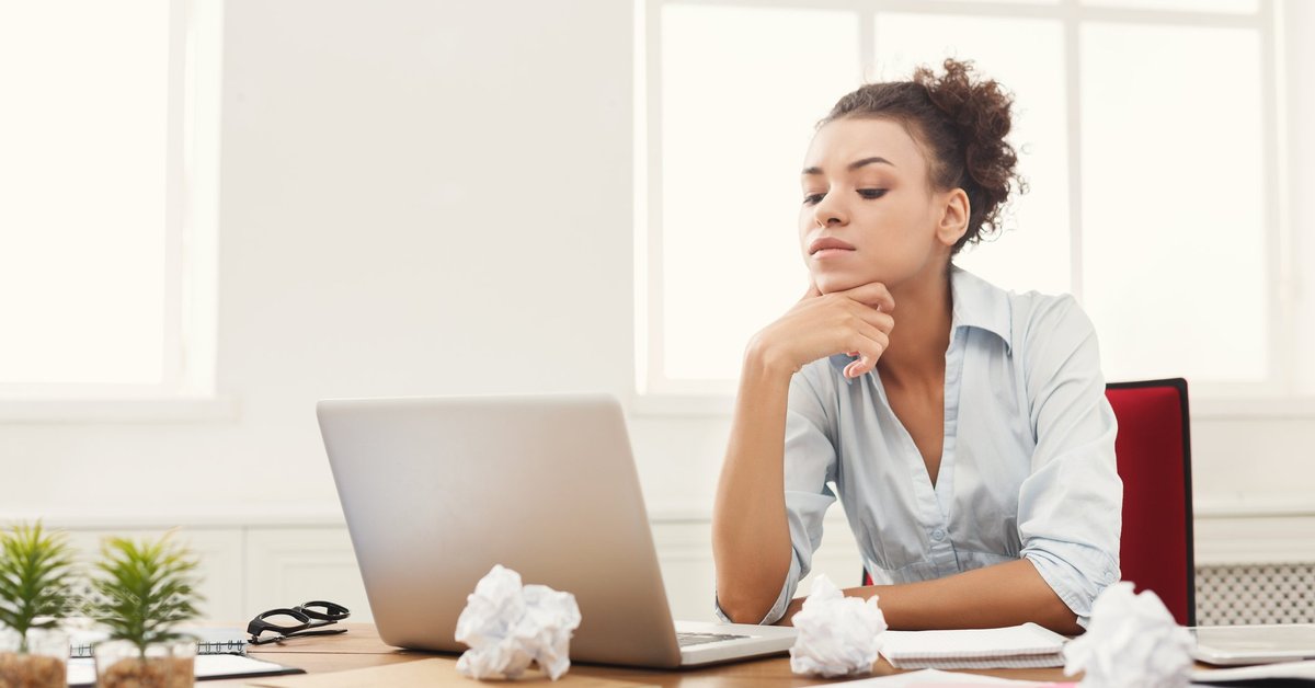 A woman looking at her laptop with papers on her desk.