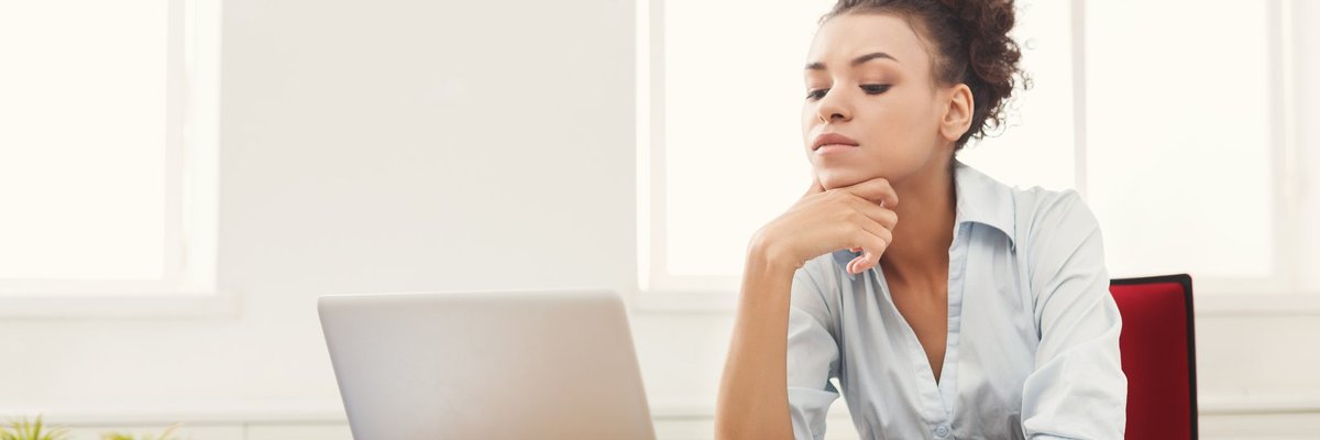 A woman looking at her laptop with papers on her desk.