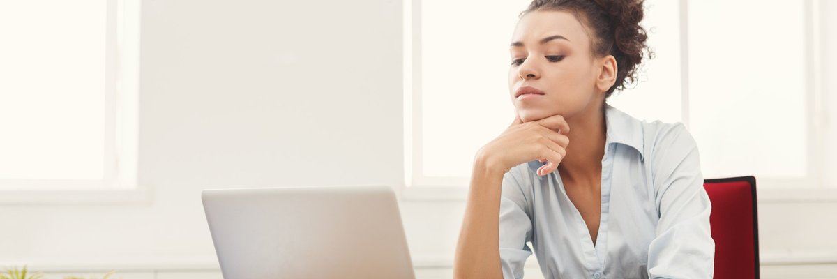A woman looking at her laptop with papers on her desk.