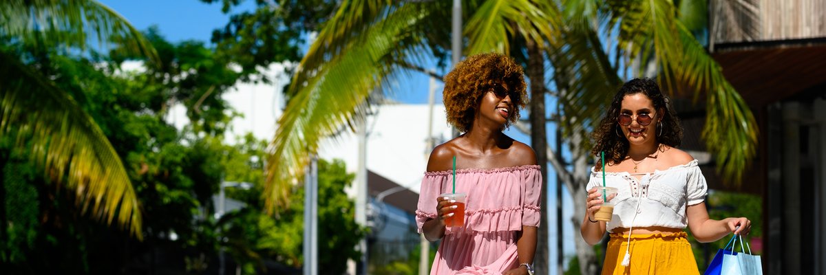 Two young women walk down a city street lined with palm trees