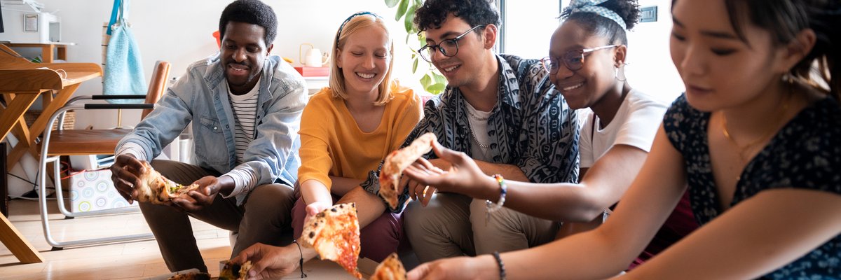 A group of friends eating pizza while sitting on the couch in an apartment.