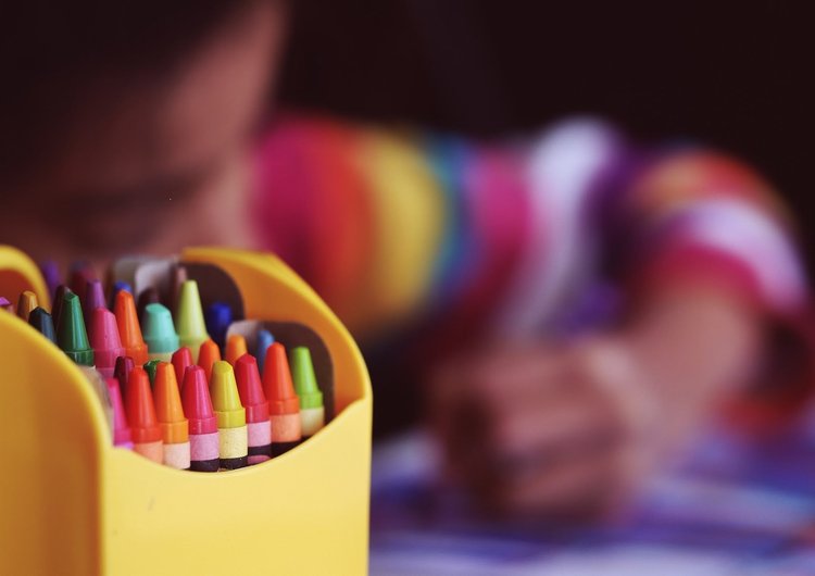 Close up view of a box of crayons with girl in the background coloring