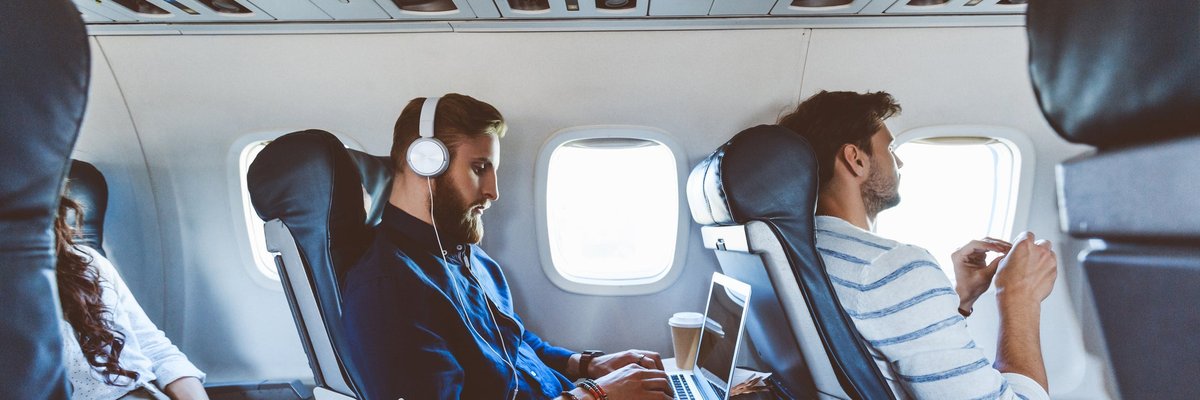Three people sitting in consecutive aisle seats on an airplane.
