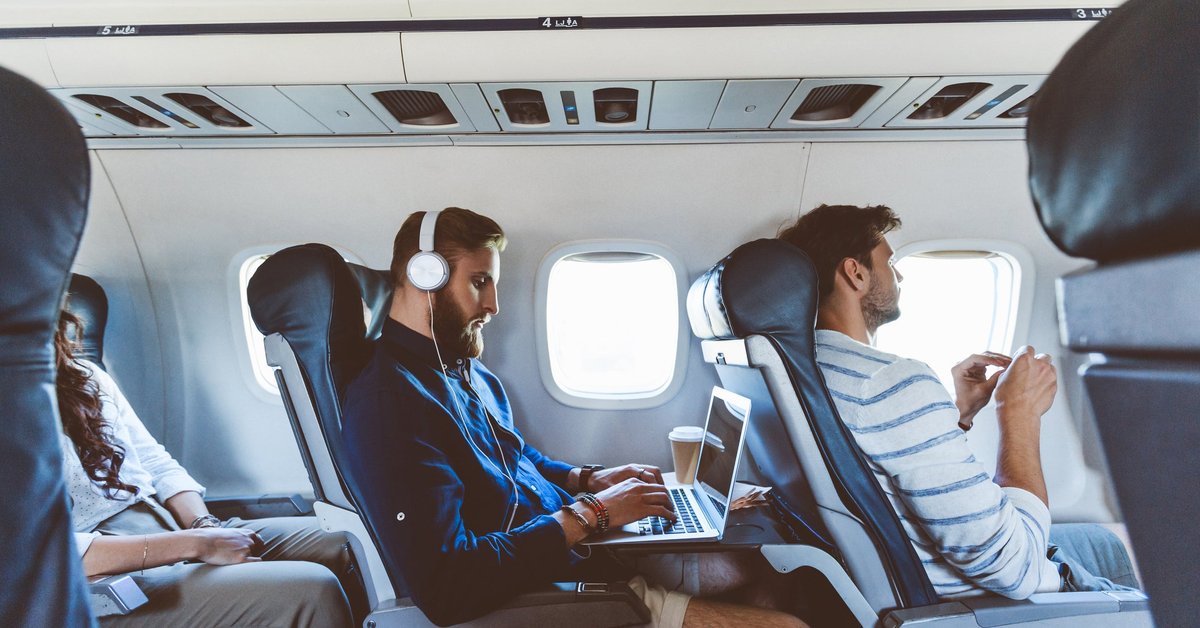 Three people sitting in consecutive aisle seats on an airplane.