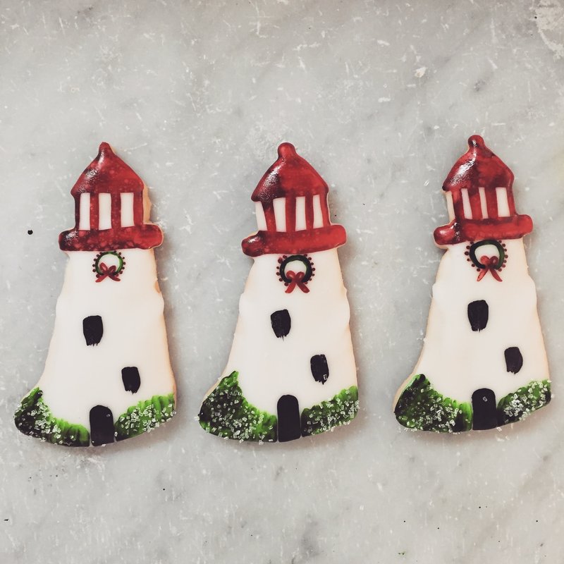 Lighthouse shaped sugar cookies decorated with royal icing to match the look of the lighthouse with a Christmas wreath.