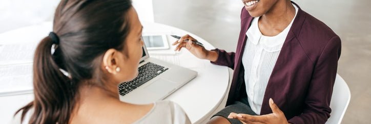 A bank representative chatting with a customer while sitting on the same side of a table.