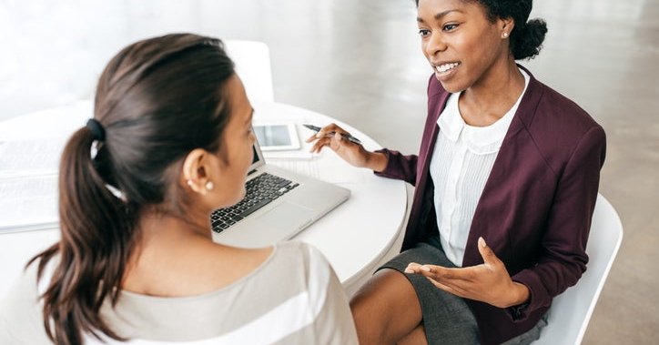 A bank representative chatting with a customer while sitting on the same side of a table.