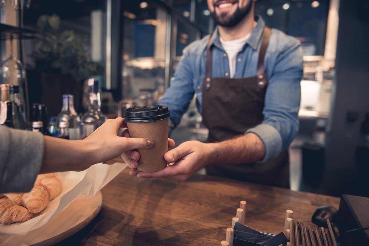 A barista handing a takeout coffee cup to a customer in a coffeeshop.
