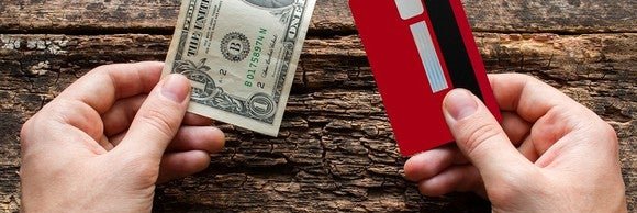 Hand holding a $1 bill and hand holding a credit card with wooden background