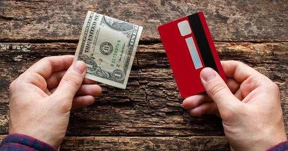 Hand holding a $1 bill and hand holding a credit card with wooden background