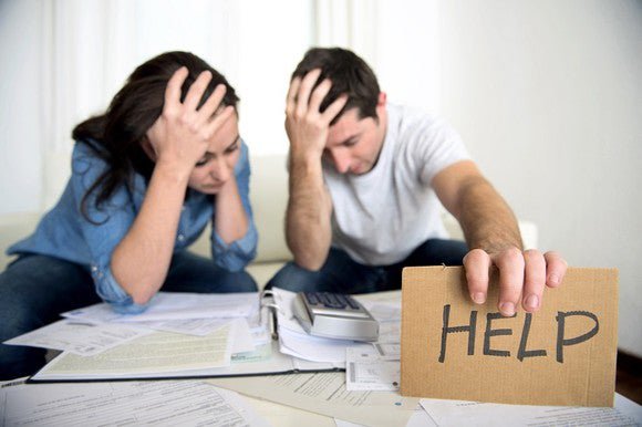 Distraught couple looking at bills holding a sign that says "help"