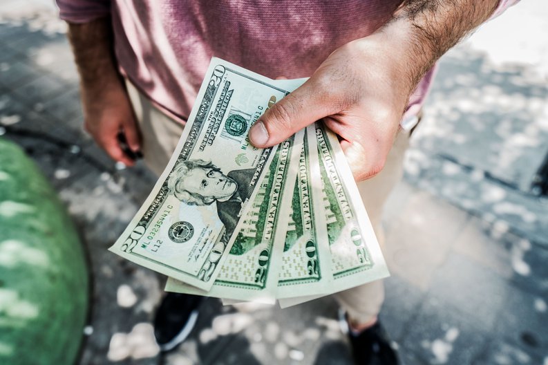 Person holding $20 bills in hand.