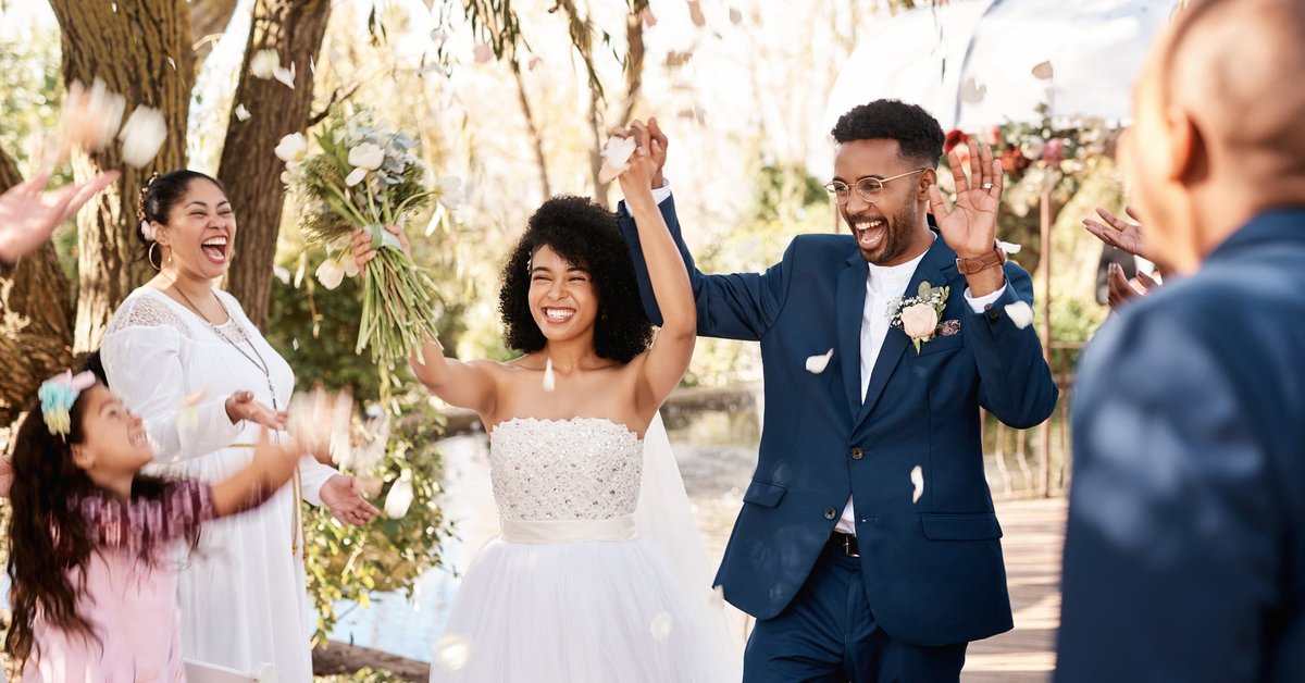 A bride and groom raising their hands and cheering while walking down the aisle after their wedding.