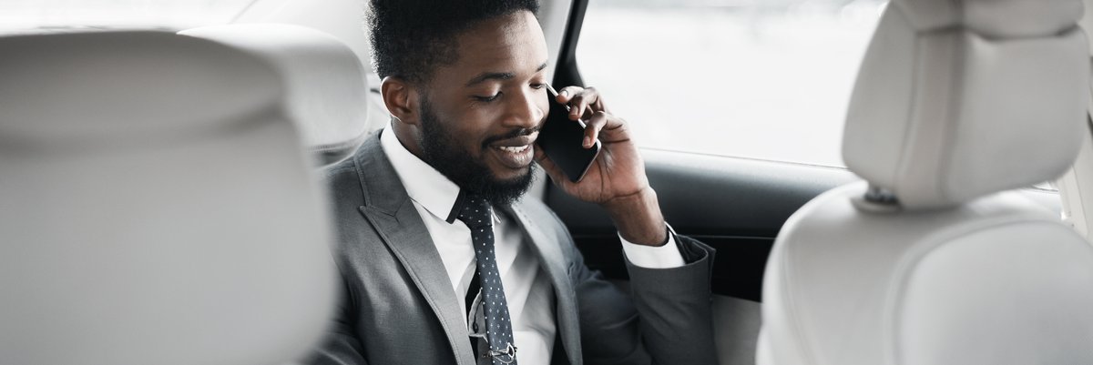 Professional wearing suit in back seat of a vehicle using his cell phone and taking notes.