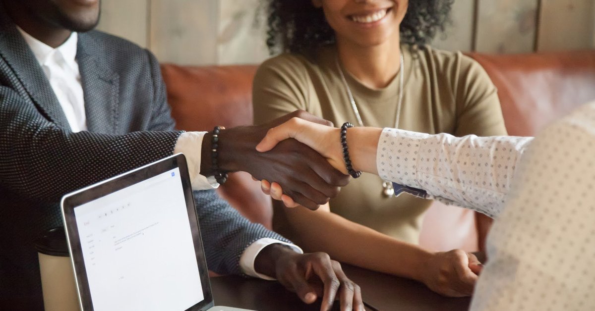 Couple shaking hands with banker over a laptop and smiling.