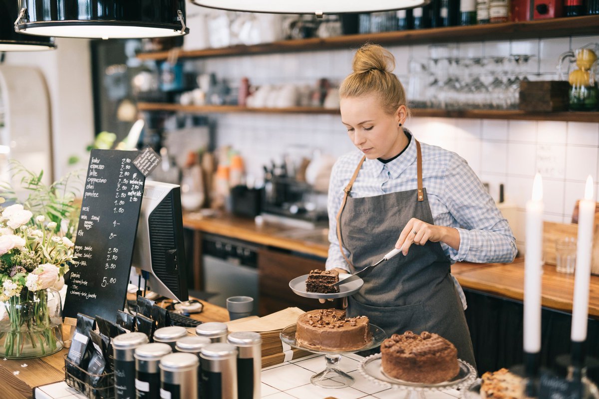 A coffeeshop worker serving a slice of cake at the cafe counter.