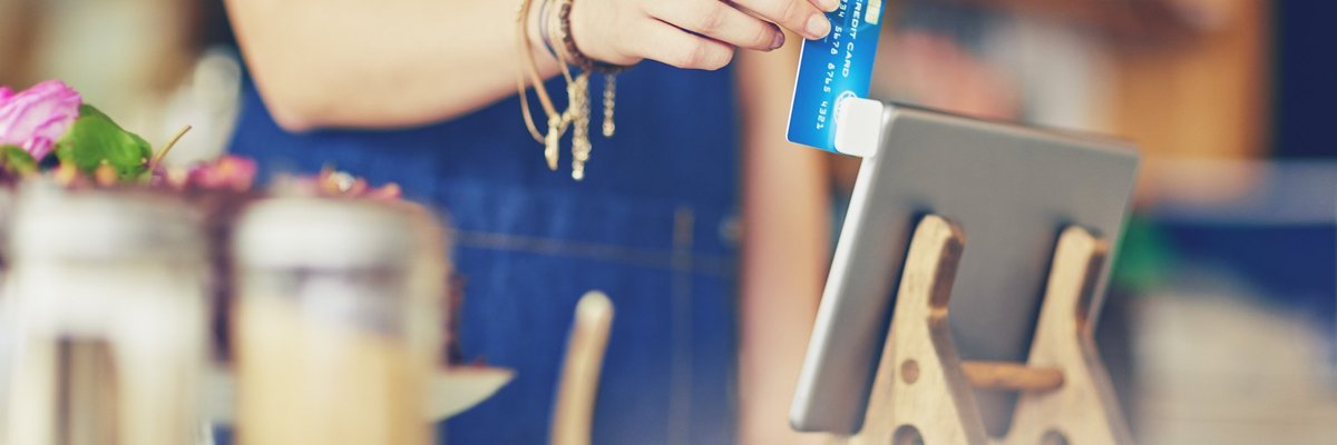 A female cashier at a restaurant swiping a credit card in a mobile card reader attached to a tablet.