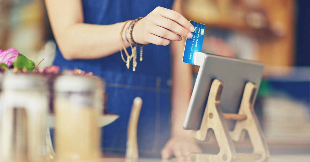 A female cashier at a restaurant swiping a credit card in a mobile card reader attached to a tablet.