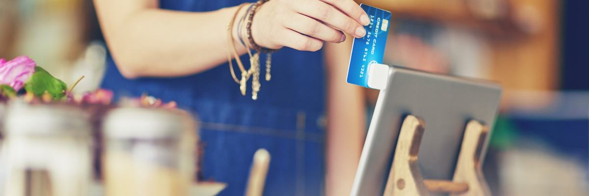 A female cashier at a restaurant swiping a credit card in a mobile card reader attached to a tablet.