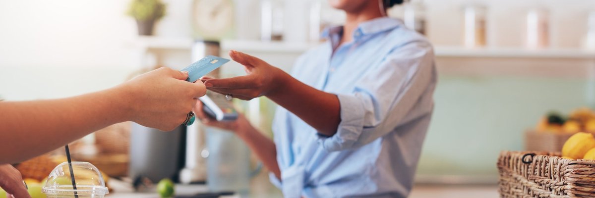 A customer handing their credit card over the counter to the cashier at a cafe.