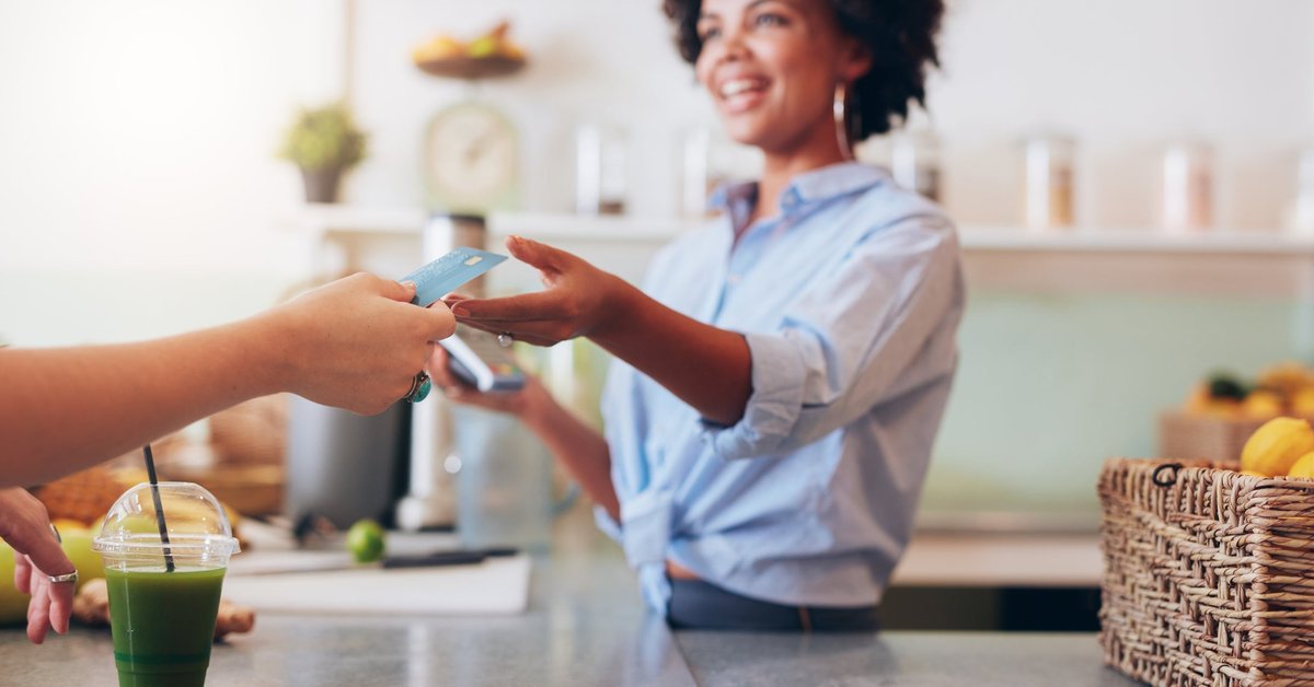 A customer handing their credit card over the counter to the cashier at a cafe.