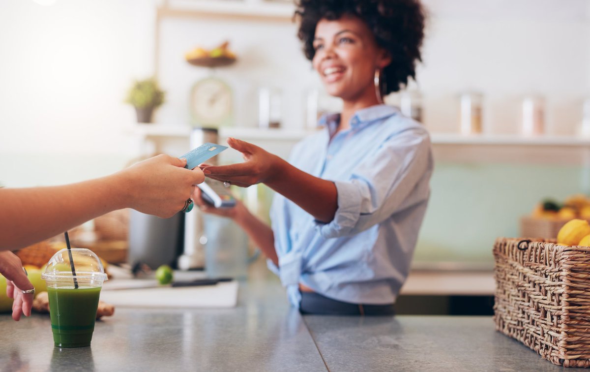 A customer handing their credit card over the counter to the cashier at a cafe.