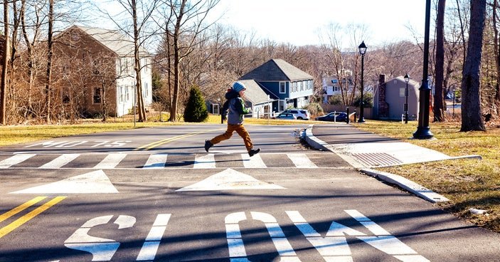 A child running across a suburban street with houses in the background and the word SLOW painted on the street in the foreground.