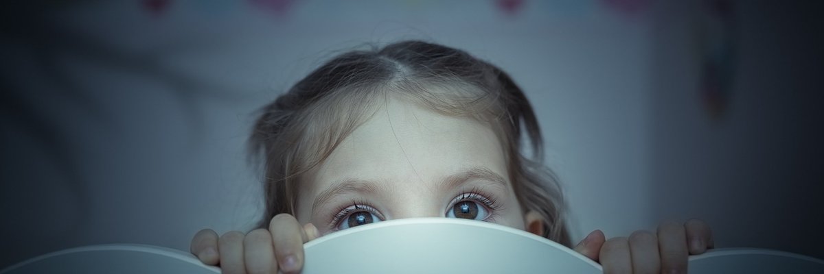 Small child peering out from behind headboard.