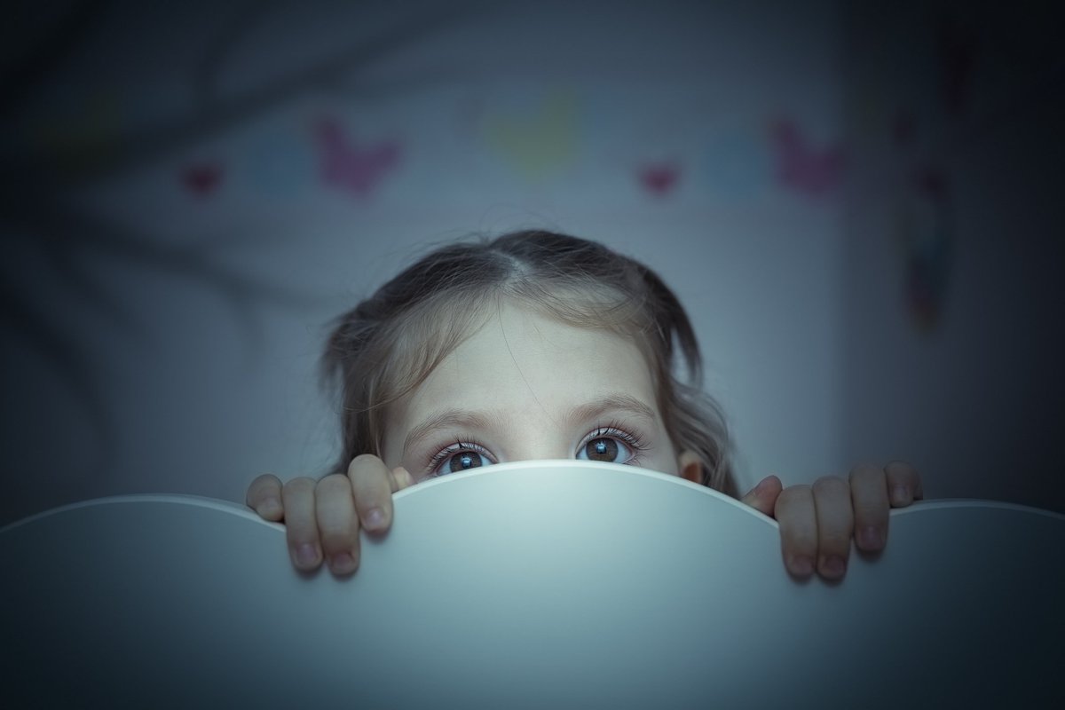 Small child peering out from behind headboard.