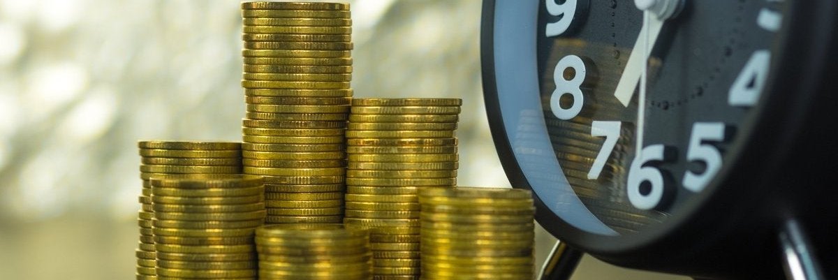 Close-up on stacks of coins sitting next to a clock