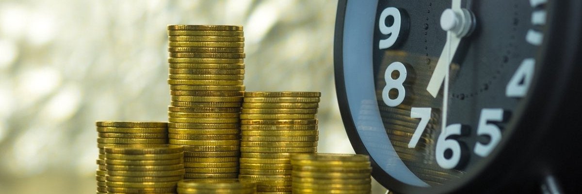 Close-up on stacks of coins sitting next to a clock